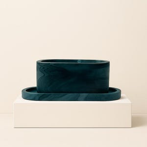 May include: A teal-colored rectangular container with rounded edges, sitting on a matching oval tray. The container and tray have a marbled appearance. The set is displayed on a white block against a neutral background.