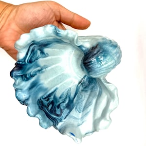 以下が含まれることがあります： 大理石模様の青と白のデザインが施された、貝殻型の装飾用セラミックボウル。 ボウルは縁が波打っており、光沢のある仕上がりで、小さなアイテムを入れたり、装飾品として最適です。 海岸をテーマにしたデザインです。