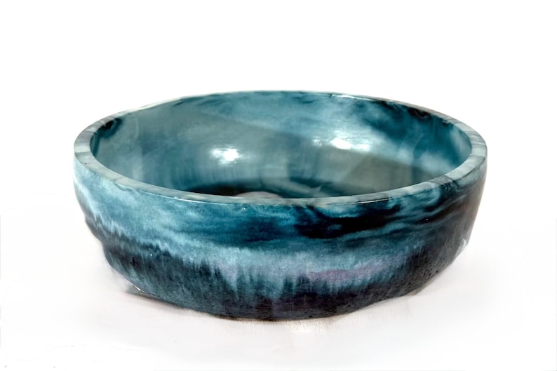 May include: A round, shallow basin with a smooth, glossy interior and a textured exterior. The surface features a blended gradient of deep navy blue at the base, transitioning into lighter shades of teal and turquoise toward the upper rim.
