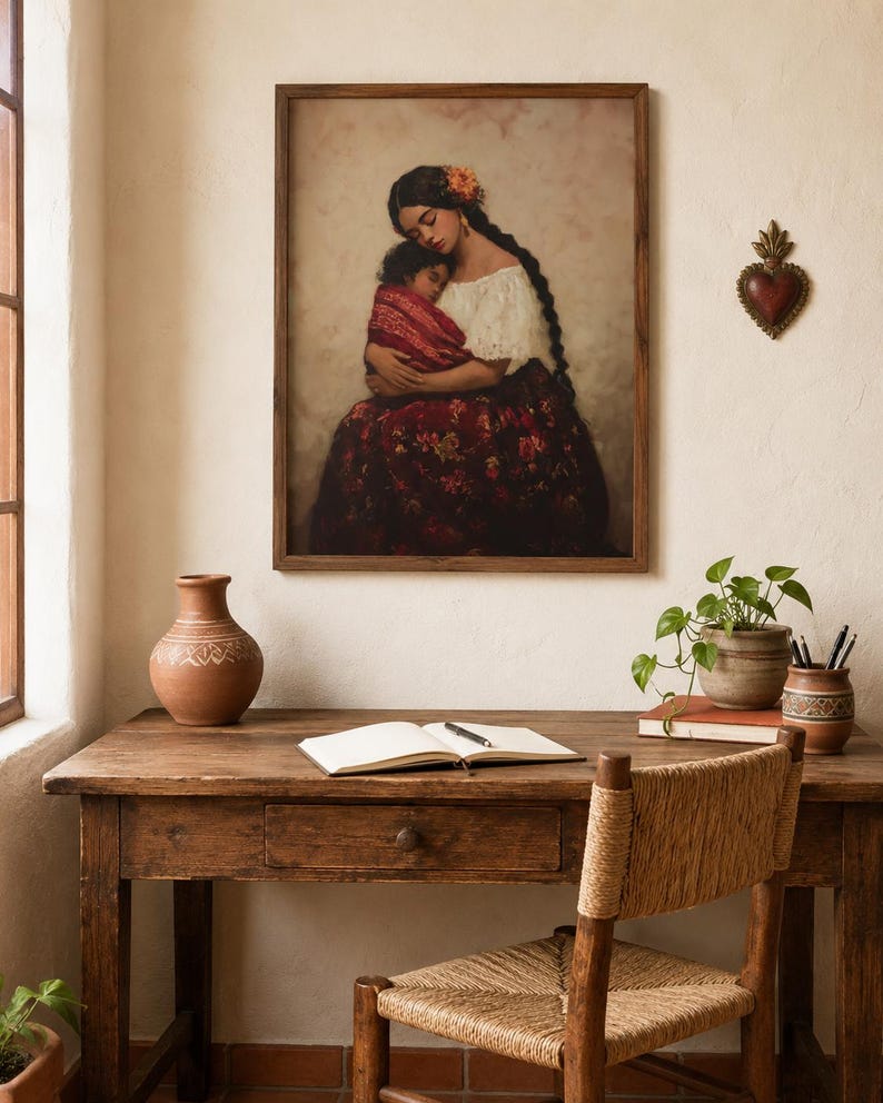 May include: A framed wall art print depicting a person with long dark braided hair holding a sleeping child, both wrapped in a red patterned textile. The person wears a white off-the-shoulder top and a dark red floral skirt against a soft background.