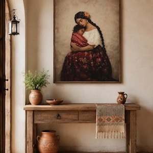 May include: A framed wall art print depicting a person with long dark braided hair wearing a white off-the-shoulder top and a dark red floral skirt, holding a child wrapped in a red patterned cloth against a neutral, textured background.