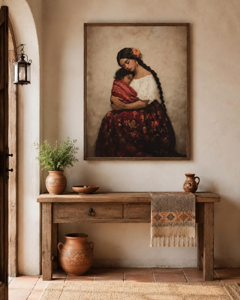 May include: A framed wall art print depicting a person with long dark braided hair wearing a white off-the-shoulder top and a dark red floral skirt, holding a child wrapped in a red patterned cloth against a neutral, textured background.