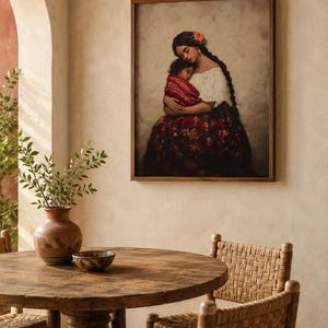 May include: A framed wall art print depicting a person with long dark braided hair wearing a white blouse and a dark red floral skirt, holding a small child wrapped in a red patterned cloth against a soft, neutral-toned background.