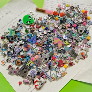 May include: A large collection of colourful metal charms, including skulls, stars, hearts, and other designs. The charms are arranged in a loose pile on a white surface.