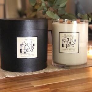 May include: Two candles with the text "San Francisco" are displayed. One is in a black cylindrical container, the other in a clear glass. Both have labels that read "Mandarin, Patchouli, Jasmine and Sea Salt."