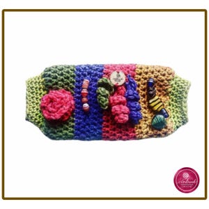 Peut inclure: Un manchon sensoriel rectangulaire en crochet avec des rayures verticales de laine verte, bleue et rose. La surface est ornée d'une fleur en crochet rose, d'une rangée de petites perles, de formes texturées en crochet et d'une perle en forme d'abeille.