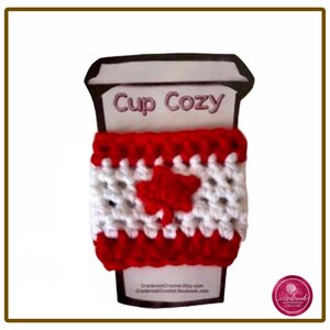 Könnte beinhalten: Ein gehäkelter Tassenwärmer mit einem rot-weiß gestreiften Muster und einem roten Ahornblatt in der Mitte auf der Vorderseite. Der Tassenwärmer ist auf einer Pappunterlage befestigt, auf der oben Cup Cozy und unten weiterer Text gedruckt ist.