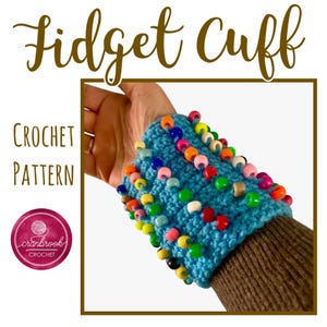 May include: A crochet pattern for a blue fidget cuff with colourful beads. The pattern is called "Fidget Cuff" and is by "Cranbrook Crochet".