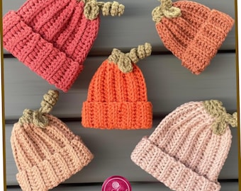 May include: Five crocheted beanies in various shades of pink and orange, each featuring a ribbed texture and a small, light green crocheted stem on top. A circular pink logo with the white text cranbrook CROCHET is positioned at the bottom center.