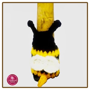 May include: A small, handmade crochet bee ornament featuring a black head with two antennae, a body with alternating horizontal black and yellow stripes, two white wings, and a yellow stinger at the base, attached to a wooden stick.