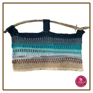 Puede incluir: Un tapiz rectangular de ganchillo suspendido de una rama de madera natural. La pieza presenta rayas horizontales en tonos verde azulado oscuro, turquesa, azul claro, gris, beige y bronceado, incorporando varios patrones de puntos texturizados.