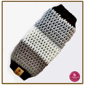 May include: A cylindrical crochet sleeve featuring horizontal stripes in black, light gray, white, and dark gray. The item has a textured, open-stitch pattern throughout and includes a small, rectangular tan leather-like brand tag on one end.