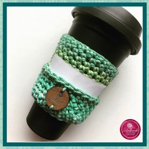 Può includere: Un copri-tazza da caffè in crochet verde e bianco con un'etichetta in legno che dice "craftbrook crochet".