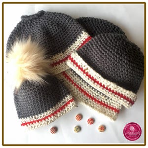 May include: Three dark grey crocheted hats with a cream and red striped band at the base. One hat features a large, fluffy beige pom-pom on top. Four small, round, patterned buttons are scattered near the bottom right of the hats.