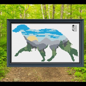 May include: A framed cross-stitch pattern featuring a dog silhouette filled with a landscape of mountains, sky, and trees. The design uses shades of blue, green, gray, and yellow. The frame is dark blue.