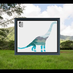 May include: A cross-stitch pattern of a blue and green dinosaur silhouette with a mountain landscape inside. The pattern is in a black frame and is ready to be downloaded as a PDF.