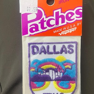 Peut inclure: Écusson thermocollant avec le mot "DALLAS" au-dessus d'un motif coloré de paysage urbain et le mot "TEXAS" en dessous. L'écusson est sur fond blanc avec une bordure violette, emballé sur un support orange. Fabriqué aux États-Unis.