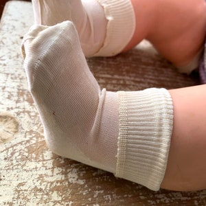 May include: A pair of white cotton socks with a ribbed cuff. The socks are worn and have a slight discoloration on the heel.