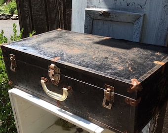 May include: A vintage black metal suitcase with brass hardware and a worn leather finish. The suitcase has a handle and two clasps.