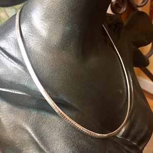May include: A silver chain necklace with a box chain design. The necklace is on a mannequin bust.