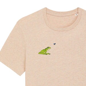 Peut inclure: Un t-shirt beige clair avec une grenouille verte et une mouche bleue brodées sur le devant.