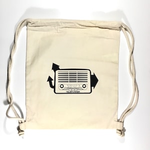 Op de afbeelding: Een crèmekleurige rugzak met trekkoord en een zwarte afbeelding van een vintage radio met het woord "TELEFUNKER" eronder. De tas heeft witte touwtjes.