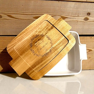 May include: A rectangular wooden serving tray with a matching lid, featuring the engraved text "that all be done in Love" within a wreath design. The tray is paired with a white ceramic baking dish, ideal for serving or baking.