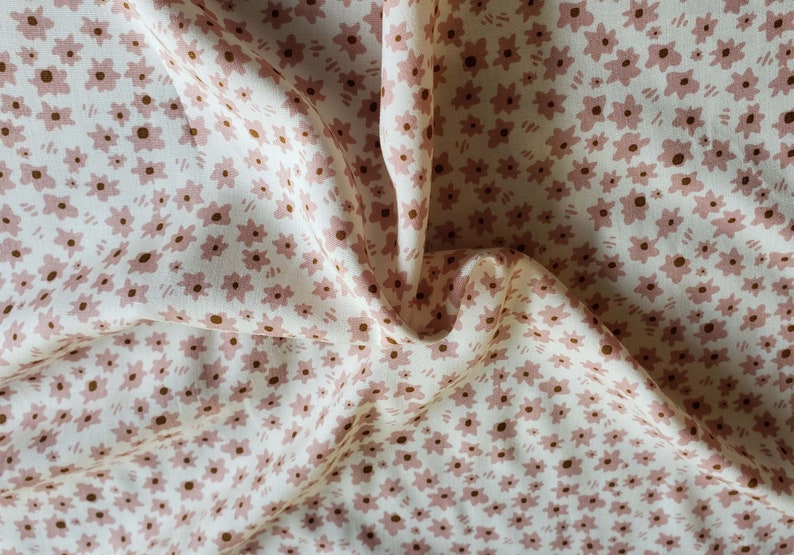 Pu&ograve; includere: Tessuto bianco con un motivo floreale rosa e marrone. Il tessuto &egrave; piegato e stropicciato.
