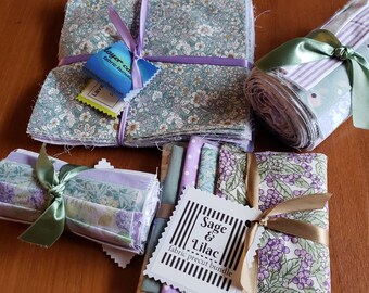 May include: Fabric bundles in various floral and patterned designs, tied with ribbons. The bundles include squares and rolled fabric, with tags attached. Colors include sage green, lavender, and white.