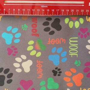 May include: Gray fabric with a repeating pattern of colorful paw prints and the word "woof" in various colors. The paw prints are in shades of pink, black, white, blue, green, and orange. A red ruler is at the top.