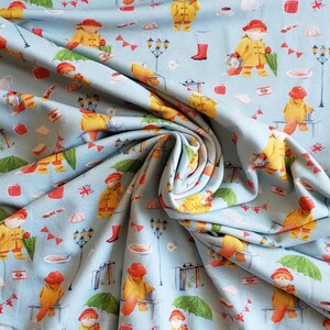 May include: Light blue fabric with a repeating pattern of a bear wearing a yellow raincoat and red hat, holding a lantern and umbrella. The design includes red boots, flags, and teacups.