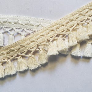 May include: Two types of white cotton trim with fringe. The trim has a delicate crocheted design and tassels.