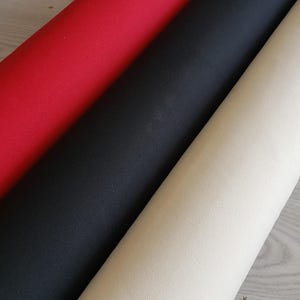 Puede incluir: Tres rollos de tela en colores rojo, negro y crema. La tela es lisa y parece ser de algod&oacute;n tejido.