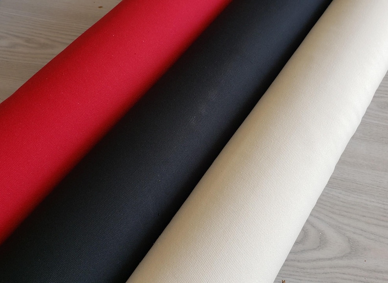 Puede incluir: Tres rollos de tela en colores rojo, negro y crema. La tela es lisa y parece ser de algod&oacute;n tejido.