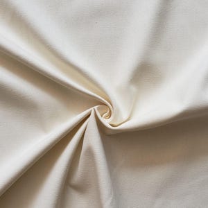 Puede incluir: Primer plano de una tela lisa de color blanco roto con una textura sutil. La tela est&aacute; doblada y drapeada, creando pliegues y curvas suaves.