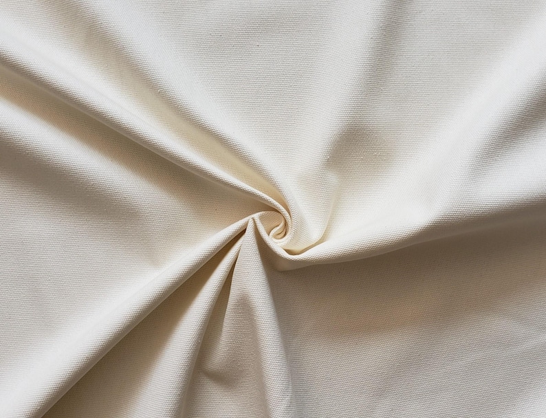 Puede incluir: Primer plano de una tela lisa de color blanco roto con una textura sutil. La tela est&aacute; doblada y drapeada, creando pliegues y curvas suaves.