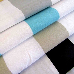 Puede incluir: Tela a rayas en blanco, gris, azul y negro. La tela está doblada en capas, mostrando los diferentes colores y patrones.