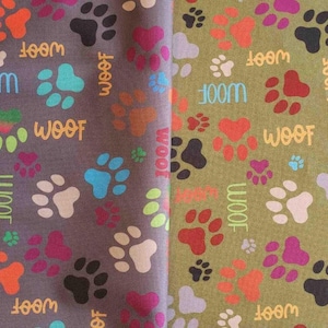 May include: Fabric with a repeating pattern of colorful paw prints and the word "WOOF" in a playful font. The paw prints are in shades of orange, pink, blue, black, and white on a gray background. The word "WOOF" is also in various colors.