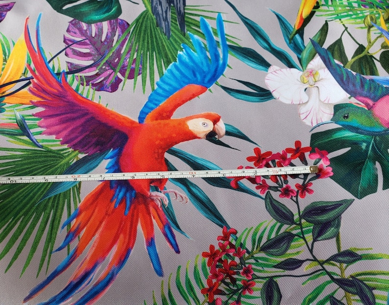 May include: A colorful tropical fabric featuring a red and blue parrot with green and purple leaves. The fabric also features a white orchid and a hummingbird.