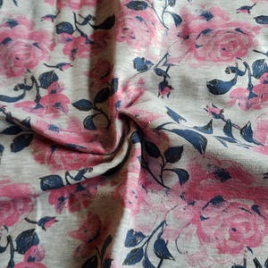 May include: Gray fabric with a pink floral print. The fabric has a soft, textured feel and is perfect for crafting projects.