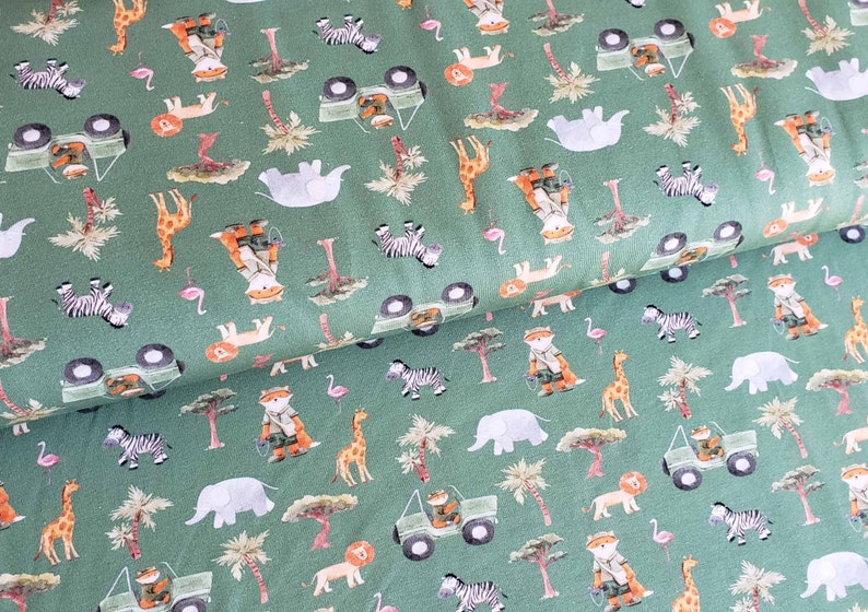 May include: Green fabric with a repeating pattern of safari animals, including zebras, giraffes, elephants, lions, and a fox in a jeep. The pattern is on a green background.