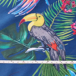 May include: A toucan with a yellow beak and black and gray feathers is perched on a branch surrounded by green tropical leaves and pink flowers on a blue background.