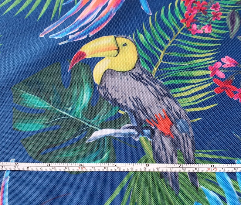 May include: A toucan with a yellow beak and black and gray feathers is perched on a branch surrounded by green tropical leaves and pink flowers on a blue background.