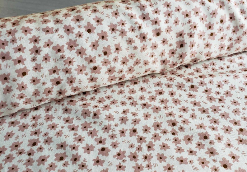 Pu&ograve; includere: Tessuto bianco con un motivo floreale rosa. I fiori sono piccoli e sparsi sul tessuto.