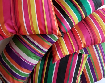 Könnte beinhalten: Ein Stapel bunter, gestreifter Kissen mit verschiedenen Farben wie Rosa, Orange, Grün, Schwarz und Weiß.