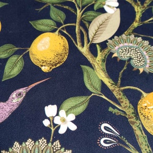 May include: A dark blue fabric with a repeating pattern of lemons, flowers, and a hummingbird. The lemons are yellow with green leaves. The flowers are white with green stems. The hummingbird is purple with a long beak.