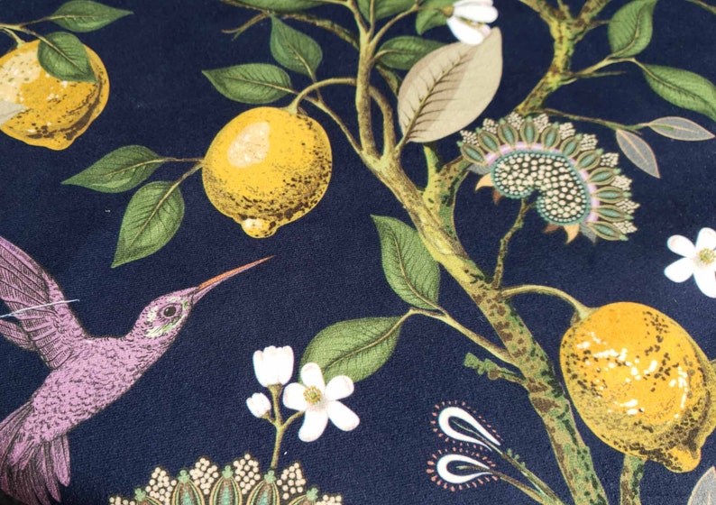 May include: A dark blue fabric with a repeating pattern of lemons, flowers, and a hummingbird. The lemons are yellow with green leaves. The flowers are white with green stems. The hummingbird is purple with a long beak.