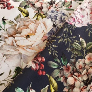 Puede incluir: Primer plano de tela floral con grandes y detalladas flores en tonos crema, rosa y burdeos sobre un fondo blanco. Una segunda sección de tela muestra flores similares sobre un fondo azul marino oscuro. Hojas verdes y bayas acentúan el diseño.
