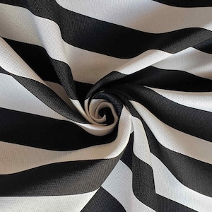 May include: Close-up of a black and white striped fabric. The fabric is folded and swirled, creating a spiral effect in the center. The stripes are thick and evenly spaced, with a slight wave pattern.