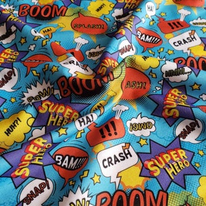May include: A blue fabric with a repeating pattern of colorful comic book speech bubbles. The bubbles contain words like "BOOM", "SUPER HERO", "SNAP", "POW", "ASH", "BAM", and "CRASH".